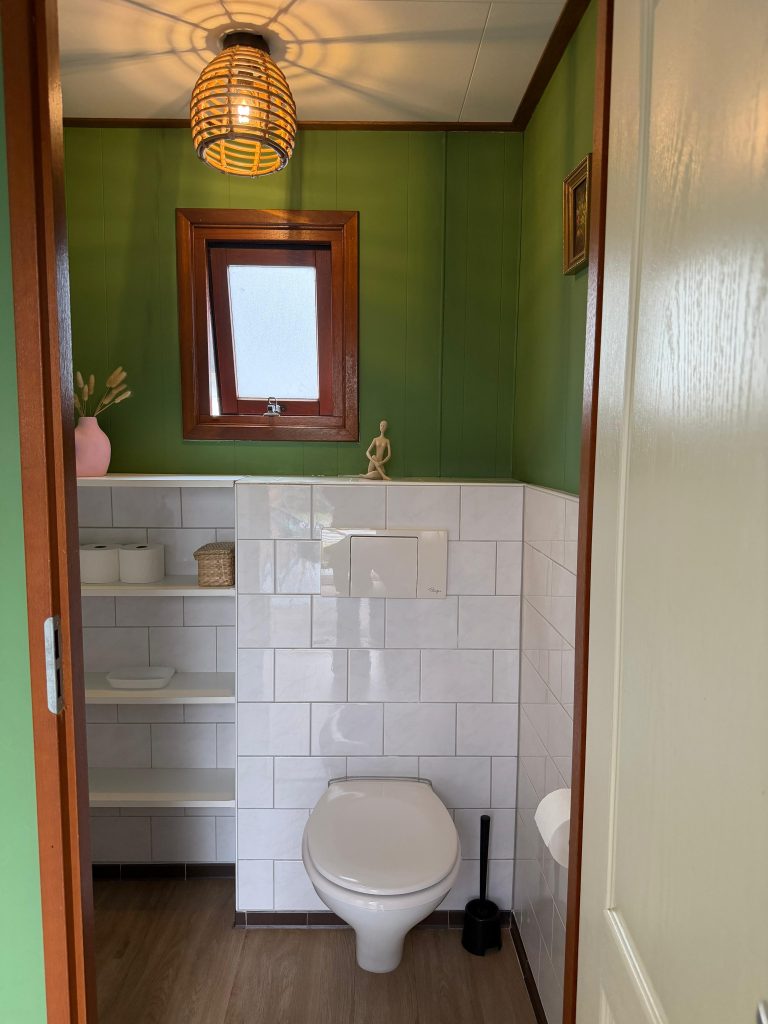 Toilet met witte tegels en houten kozijn